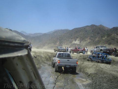 1987 Suzuki Samurai - Several off-road vehicles navigate a muddy trail with steep hills in the background.
