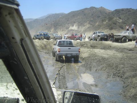 1987 Suzuki Samurai - Off-road vehicles navigate a challenging muddy terrain, with one truck requiring assistance.
