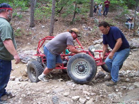 1989 Ford Bronco II - Men push a red off-road buggy through a rocky, wooded area.