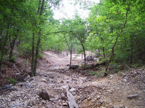1989 Ford Bronco II - Two off-road vehicles navigate a challenging rocky trail through a dense forest.