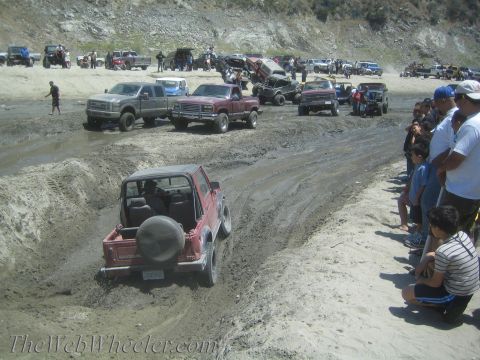1987 Suzuki Samurai - A group of off-road vehicles navigate a muddy course, with a red Suzuki Samurai in the foreground.