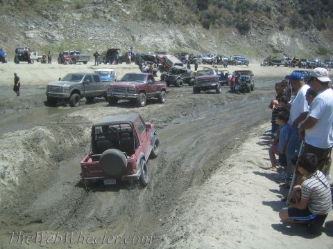 1987 Suzuki Samurai - A crowd watches as a red 1987 Suzuki Samurai navigates a muddy track alongside other off-road vehicles.