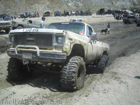 1987 Suzuki Samurai - A heavily modified GMC pickup truck navigates a muddy off-road course with other vehicles in the background.