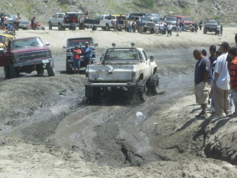 1987 Suzuki Samurai - A white pickup truck navigates a muddy track with onlookers watching from the side.