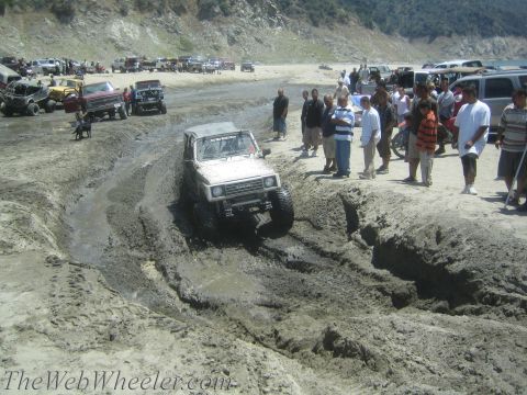 1987 Suzuki Samurai - Suzuki Samurai tackles a challenging mud pit with a crowd gathered to observe.