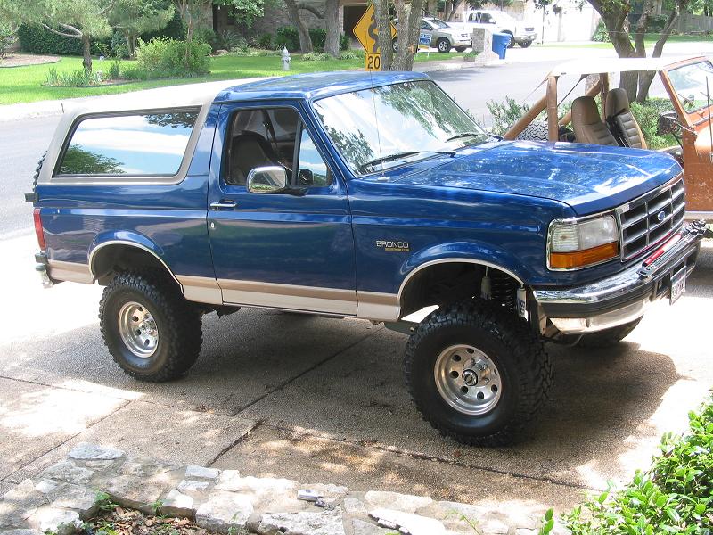Blue and tan lifted Ford Bronco SUV on chunky tires, parked in driveway, 3/4 front view