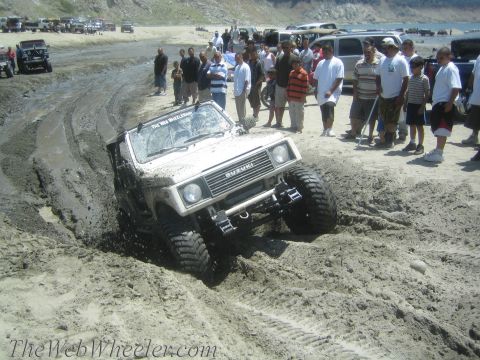 1987 Suzuki Samurai - A modified Suzuki Samurai tackles a challenging muddy terrain, with a crowd gathered to observe the off-road action.