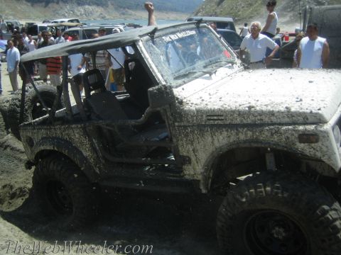 1987 Suzuki Samurai - Muddy 1987 Suzuki Samurai navigating a rough terrain with spectators nearby.