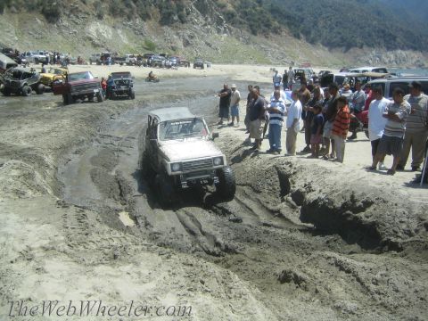 1987 Suzuki Samurai - A Suzuki Samurai navigates a muddy track while onlookers observe the off-road action.