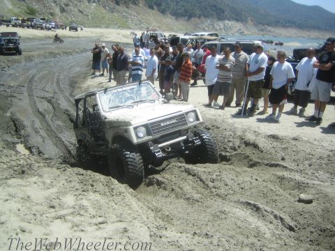 1987 Suzuki Samurai - Suzuki Samurai navigating a muddy trail with a crowd gathered on the bank.