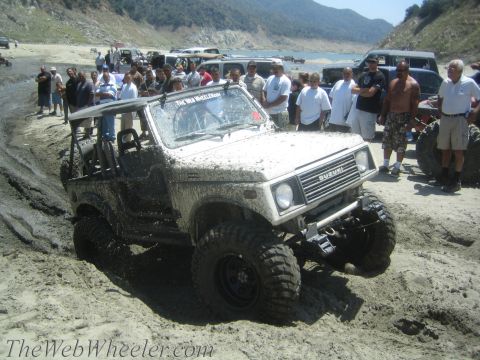 1987 Suzuki Samurai - A group of people watch as a Suzuki Samurai gets stuck in the mud near a body of water.