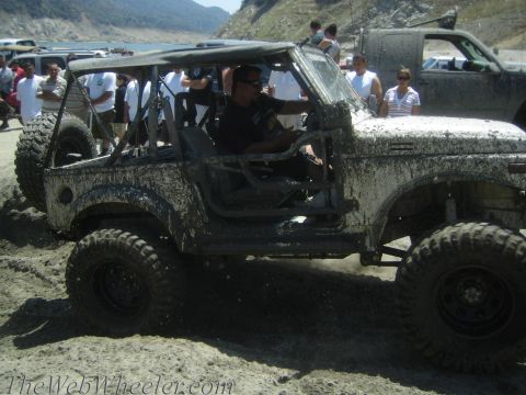 1987 Suzuki Samurai - A 1987 Suzuki Samurai navigates a muddy terrain with onlookers in the background.