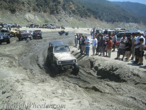 1987 Suzuki Samurai - A Suzuki Samurai tackles a challenging muddy terrain, observed by a crowd of onlookers at an outdoor event.