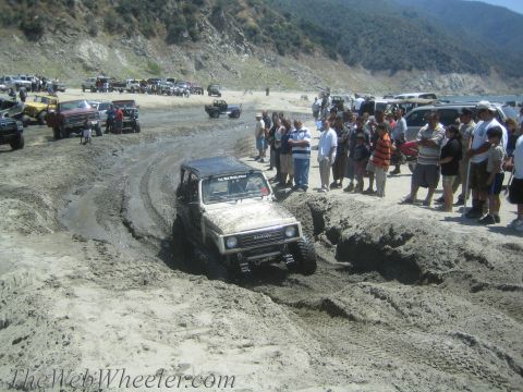 1987 Suzuki Samurai - Suzuki Samurai tackles a challenging muddy course with a crowd observing the action.
