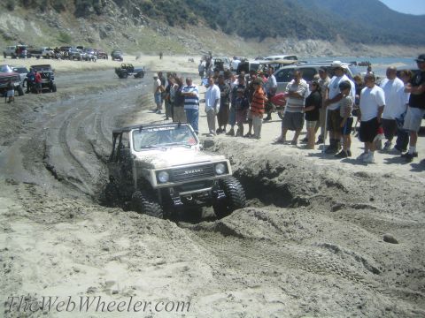 1987 Suzuki Samurai - A Suzuki Samurai navigates a challenging muddy terrain, with a crowd gathered to observe the off-road action.