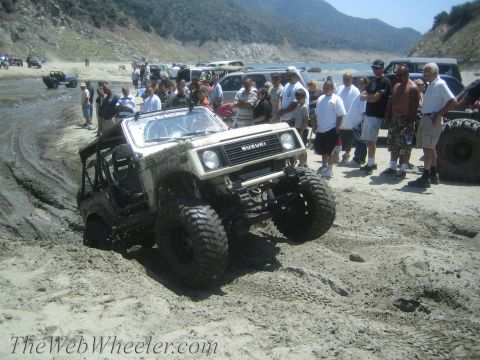 1987 Suzuki Samurai - A modified Suzuki Samurai navigates a muddy terrain with onlookers present.