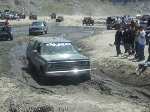 1987 Suzuki Samurai - A group of off-road vehicles navigate a muddy terrain, with one Suburban struggling to move forward.