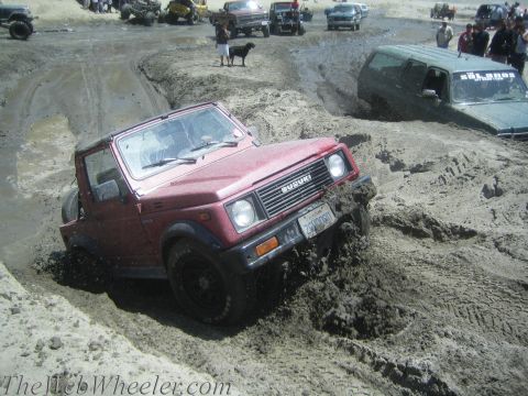 1987 Suzuki Samurai - A red 1987 Suzuki Samurai navigates a muddy off-road course, with other vehicles visible in the background.
