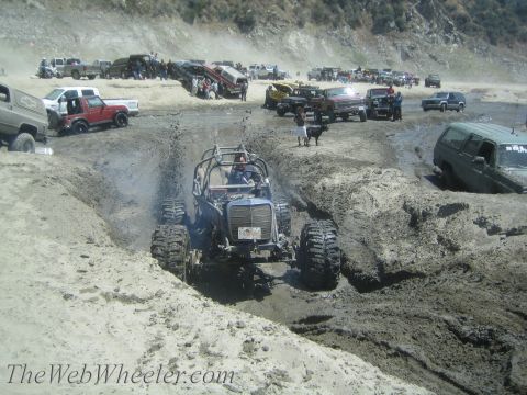 1987 Suzuki Samurai - Off-road buggy navigating a challenging mud pit with multiple vehicles and onlookers present.