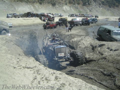 1987 Suzuki Samurai - Multiple off-road vehicles are seen navigating a muddy terrain with spectators watching from the sidelines.