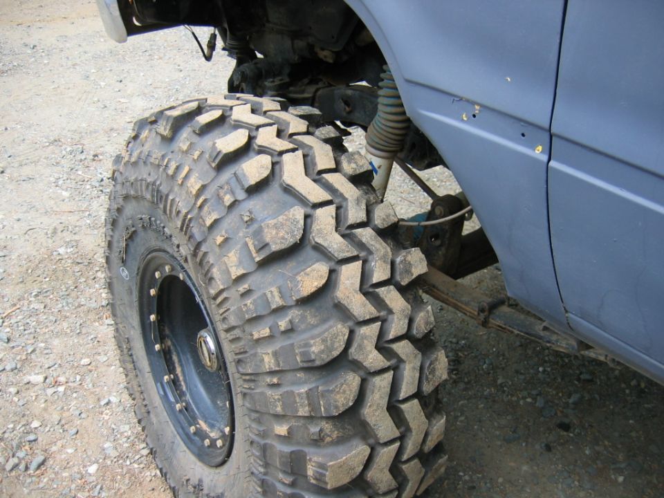 Muddy off-road tire on a vehicle with blue body panel and visible suspension