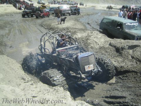 1987 Suzuki Samurai - A custom off-road buggy navigates a muddy terrain, with spectators and other vehicles gathered nearby.