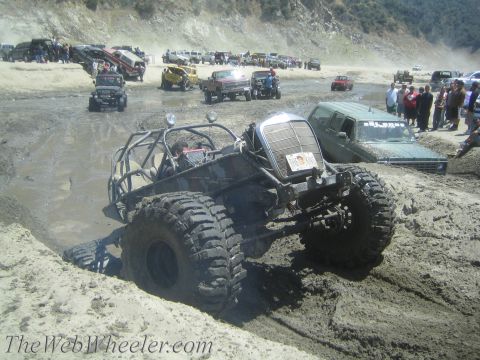 1987 Suzuki Samurai - A custom buggy tackles a muddy obstacle course with numerous other off-road vehicles gathered.