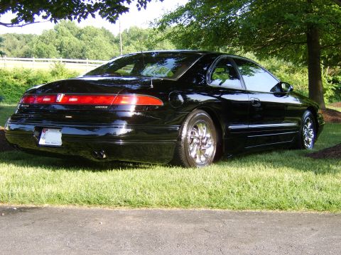 1996 Mercury Grand Marquis - Rear view of a black Lincoln Mark VIII coupe parked on a grassy lawn under trees.
