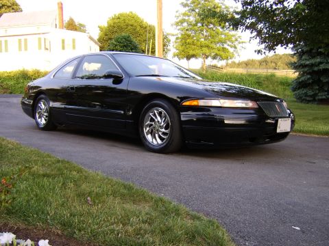 1996 Mercury Grand Marquis - A black coupe with chrome wheels sits on a driveway, with a house and trees visible.