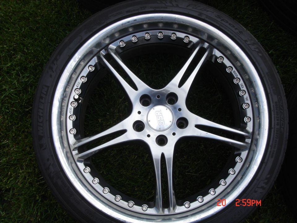 Chrome SSR wheel with five split spokes and a black tire on grass