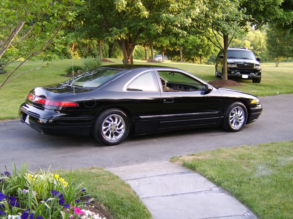 Black coupe parked in driveway, rear three-quarter view, with chrome wheels