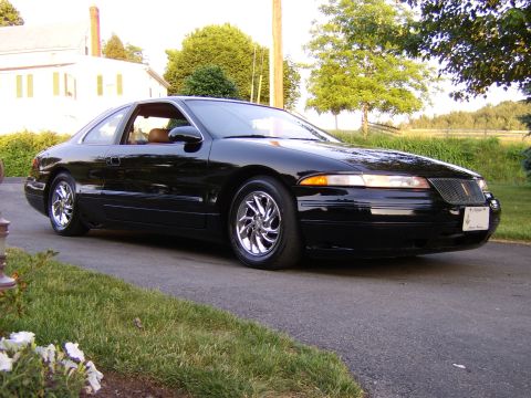 1996 Mercury Grand Marquis - A black coupe with a distinctive grille sits parked on a paved driveway, with a house and trees in the background.