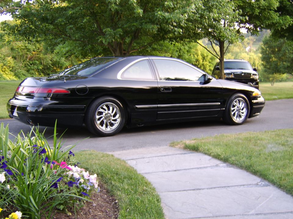 Black coupe parked in driveway, rear 3/4 view with chrome wheels