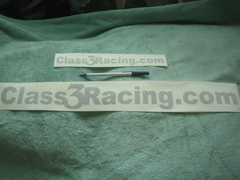 Two gray 'Class3Racing.com' vinyl decals beside a pen on green towel