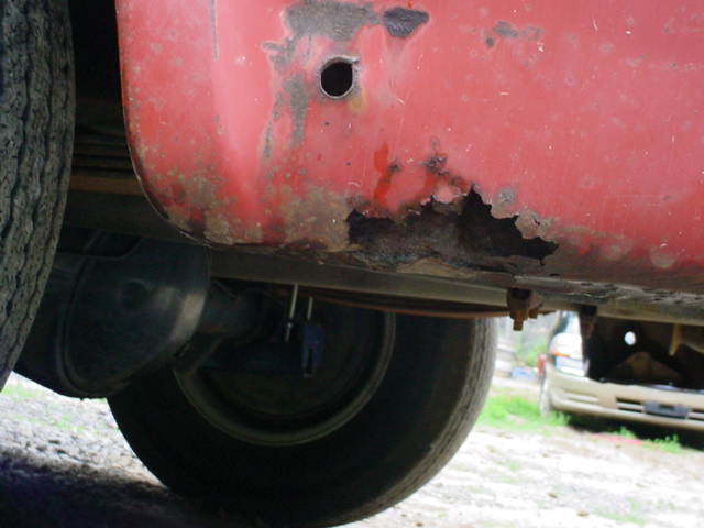 Rusted lower body panel of a faded red pickup above the rear wheel