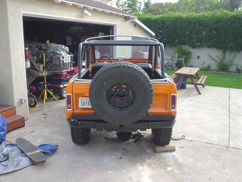 1977 Ford Bronco - Rear view of an orange 1977 Ford Bronco, a spare tire on the tailgate and a roll cage.