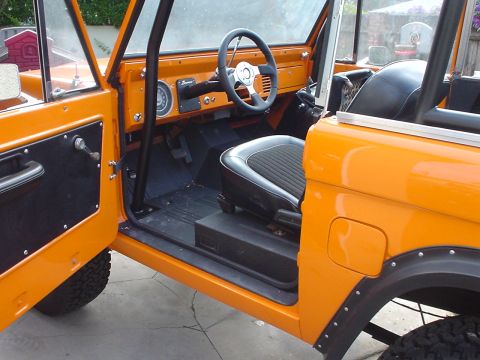 1977 Ford Bronco - The interior of this 1977 Ford Bronco features black seats, a roll cage, and a custom steering wheel.