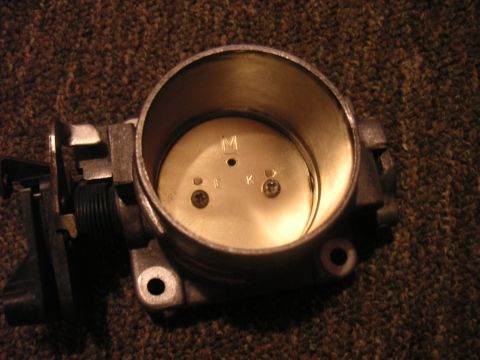 1996 Ford Crown Victoria - A throttle body part is shown, with visible markings and screws, on a carpeted surface.