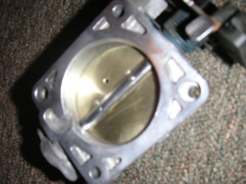 Throttle body with a metal butterfly valve inside, resting on a carpeted surface