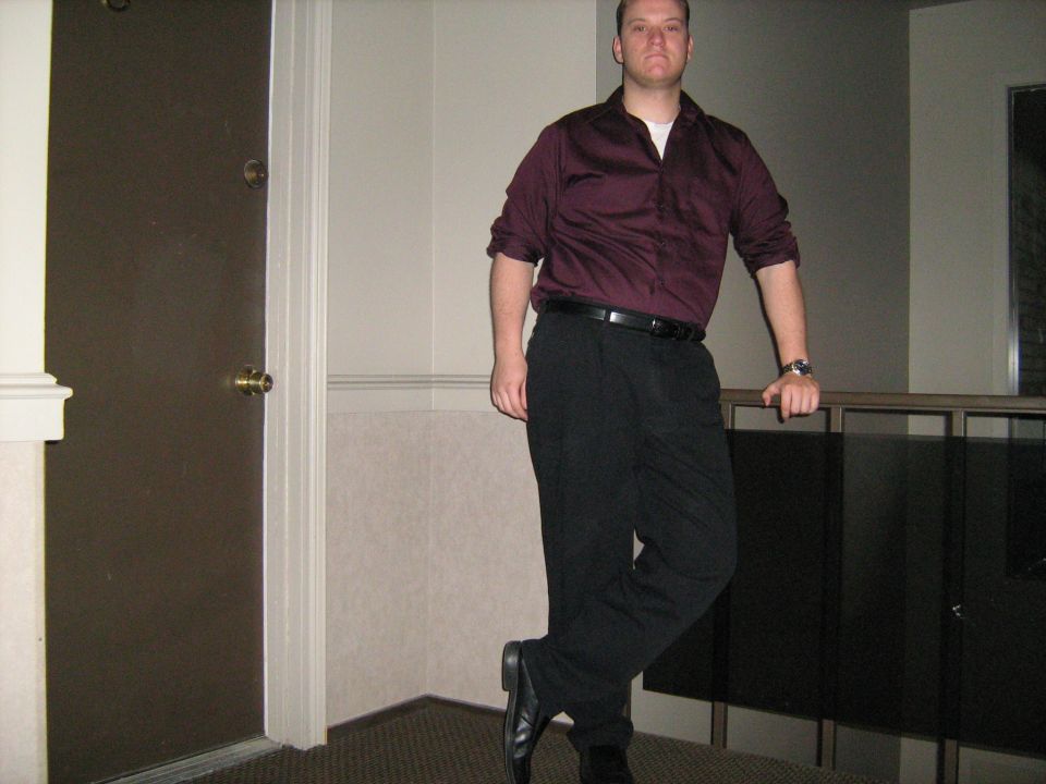 Man in a maroon shirt and black pants standing by a railing indoors