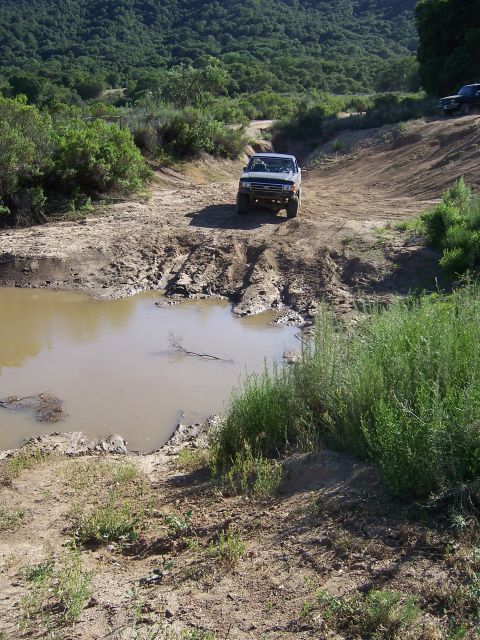 1991 Ford Bronco - An off-road vehicle navigates a challenging muddy terrain on a sunny day.