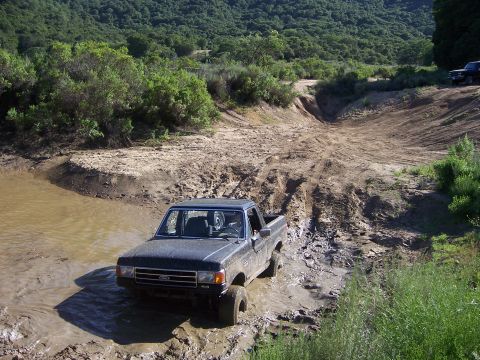 1991 Ford Bronco - Ford F-150 pickup truck driving through a muddy off-road course.
