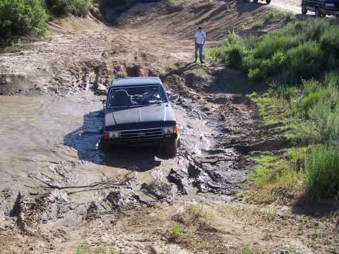 1991 Ford Bronco - A dark SUV attempts to drive through a muddy terrain, with another vehicle visible on the hill above.