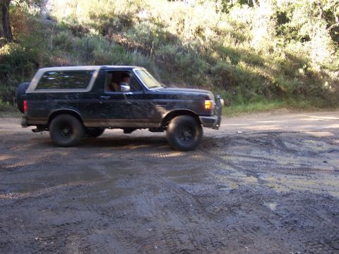 1991 Ford Bronco - A black 1991 Ford Bronco navigates a muddy, tire-tracked dirt road.