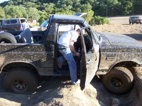 1991 Ford Bronco - A muddy 1992 Ford Bronco is partially stuck in the dirt, with a person entering the driver's side.