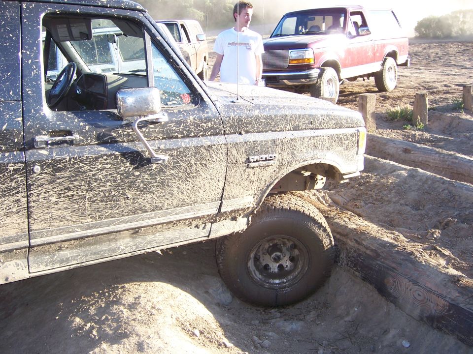 Mud-covered 1991 Ford Bronco driving over logs with another Bronco behind it