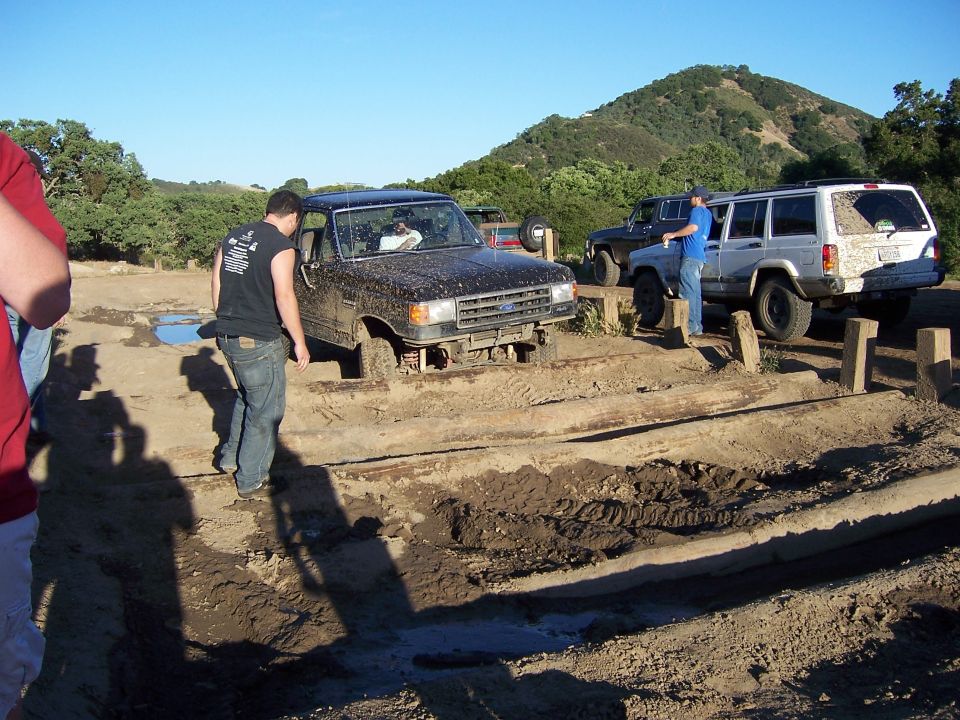Black Ford Bronco stuck in mud on wooden obstacle course