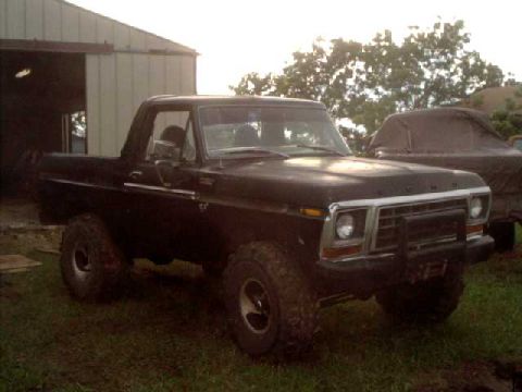 1978 Ford Bronco - A black 1978 Ford Bronco is parked outside a building with another vehicle covered in a tarp in the background.