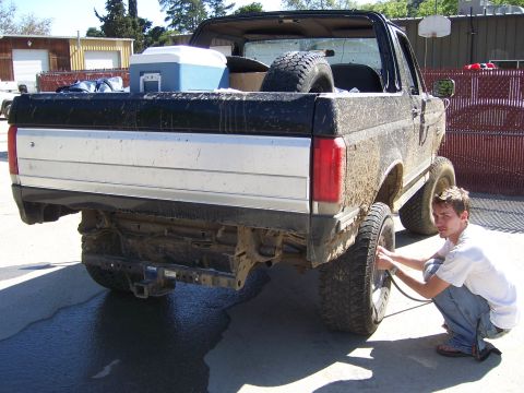 1991 Ford Bronco - Man airing up the tire of a mud-covered 1991 Ford Bronco.