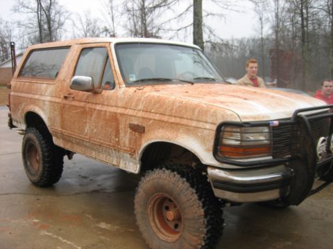 1996 Ford Bronco - A heavily muddied 1992 Ford Bronco sits on a paved area, its off-road modifications visible.